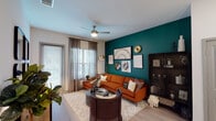Located at 14175 Dallas Pkwy in Farmers Branch, Texas, this single-floor residence offers a thoughtfully designed layout with stylish, contemporary finishes throughout. The living area serves as the centerpiece of the home, featuring a striking deep teal accent wall adorned with curated artwork, light wood-style flooring, and large windows dressed in sheer drapes that invite abundant natural light. A ceiling fan adds comfort, while a sliding glass door provides access to the outdoors. The kitchen is both functional and elegant, showcasing white shaker cabinetry, granite countertops, a large island with an undermount sink and pendant lighting, a classic subway tile backsplash, and a full suite of stainless steel appliances. The bedroom is a calm retreat, appointed with plush carpeting, oversized windows with rich teal drapes, a ceiling fan, and warm, neutral tones. The bathroom continues the refined aesthetic with granite vanity surfaces, white cabinetry, wood-style flooring, a marble-surround shower, and direct access to a spacious walk-in closet with built-in shelving and hanging rods. Throughout the residence, cohesive design choices and quality finishes create an inviting, modern atmosphere suited for comfortable living.