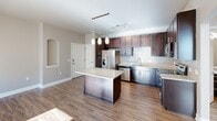 Located at Spire in Colorado Springs, CO, this one-bedroom, one-bathroom residence delivers a well-designed, single-floor layout with thoughtful finishes and functional living spaces. The open-concept living, dining, and kitchen area is bright and inviting, featuring warm hardwood-style flooring, neutral wall tones, and a ceiling fan. A charming arched niche adds an architectural accent to the main living area. The kitchen is a standout, showcasing rich dark espresso cabinetry that reaches the ceiling for ample storage, granite countertops, a central island with pendant lighting, a subway tile backsplash, and a full suite of stainless steel appliances including a refrigerator with ice maker, dishwasher, microwave, and range. The bedroom is comfortably sized with soft carpet flooring, a ceiling fan, and a natural light-filled window with blinds. It includes access to a walk-in closet as well as an additional closet. The bathroom features a granite-topped vanity with dark cabinetry, a large mirror, and a full tub-shower combo with hardwood-style flooring. Additional highlights include a private balcony, in-unit laundry, and a hallway connecting all spaces seamlessly for a cohesive, comfortable living experience.