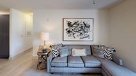 This single-floor residence offers a thoughtfully designed open-concept layout that seamlessly connects the kitchen, dining, and living areas. The kitchen is outfitted with dark, flat-front cabinetry, granite countertops, stainless steel appliances including a range, microwave, and refrigerator, all set atop light wood-style flooring that extends throughout the main living spaces. A kitchen island provides additional prep and seating space, while track lighting illuminates the open dining and living area, where large-scale artwork adds a contemporary touch.

The living room is a comfortable and stylish retreat, featuring a generously sized sectional sofa, layered accent pillows, and large windows dressed with patterned curtains and wood blinds that invite natural light and outdoor views of surrounding greenery.

The bedrooms are carpeted and serene, each featuring natural light through window treatments, and one bedroom includes direct access to a spacious walk-in closet. The primary bedroom is elegantly appointed with a ceiling fan and ample room for furnishings.

Two bathrooms serve the residence. The primary bathroom features dark cabinetry with a granite-topped vanity, a tub-shower combination, and wood-look tile flooring. The secondary bathroom offers a granite vanity with gray cabinetry and light, neutral finishes throughout. Together, these spaces deliver a cohesive, modern aesthetic.