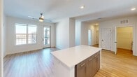 Located at 1803 S 46th St in Rogers, Arkansas, this well-designed one-bedroom, one-bathroom unit offers a thoughtful layout across a single floor. The open-concept living and kitchen area serves as the heart of the home, anchored by a large center island with crisp white quartz countertops and gold-toned hardware. The kitchen is equipped with stainless steel appliances including a refrigerator, electric range, over-the-range microwave, and dishwasher, all complemented by a two-tone cabinetry scheme — white upper cabinets paired with gray lower cabinets — and a classic white subway tile backsplash. Light hardwood-style flooring flows throughout the main living areas, while recessed lighting and a ceiling fan add both function and style. Glass doors open to a private balcony, inviting natural light into the living space. The bedroom features plush carpeting, a ceiling fan, and a window with outdoor views. The bathroom connects directly to a dedicated closet with wire shelving for organized storage. A separate laundry room houses a full-size washer and dryer with additional overhead shelving, providing convenient in-unit laundry. The overall aesthetic is clean, contemporary, and move-in ready.