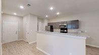 Located at 3151 Boulevard De Sevilla Blvd in Foley, Alabama, this single-story home offers a clean, contemporary design with a neutral color palette and consistent finishes throughout. The kitchen is a standout feature, equipped with dark gray cabinetry, granite-style countertops, a breakfast bar peninsula, and a full suite of stainless steel appliances including a refrigerator, range, and microwave. Light wood-style luxury vinyl plank flooring extends through the main living and kitchen areas, creating a cohesive and easy-to-maintain aesthetic. The open living area is accented by a ceiling fan with light fixture, recessed lighting, and natural light from multiple windows fitted with blinds. Bedrooms are carpeted for comfort, with at least one featuring a walk-in closet with built-in shelving and rod, as well as windows that bring in natural light. The bathroom includes a granite-topped dark vanity, a full tub-shower combination, and matching wood-look tile flooring. Throughout the home, white panel doors, clean baseboards, and neutral warm-toned walls contribute to a move-in-ready, well-finished living environment.