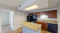Located at 1400 Village Blvd in West Palm Beach, Florida, this one-bedroom, two-bathroom residence offers a thoughtfully designed single-floor layout. The kitchen is a standout feature, showcasing rich medium-toned wood cabinetry, striking gold-veined granite countertops, and a central island that provides additional prep and dining space. Light wood-style flooring runs throughout, and black appliances including a refrigerator, range, and dishwasher complete the functional setup. A skylight-style ceiling fixture adds brightness to the kitchen area. The bedroom is comfortably carpeted and features a ceiling fan with light, a window dressed with blinds that allows natural light and outdoor views, and a generous walk-in closet equipped with built-in wire shelving for organized storage. An in-unit washer is conveniently located adjacent to the closet. The bathrooms include a tiled tub-and-shower combination with a classic white tile surround accented by a warm tan border detail and louvered closet doors nearby. Neutral tones and clean finishes throughout create a cohesive, easy-to-personalize living environment suited for comfortable everyday living in West Palm Beach.