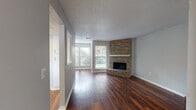 This single-floor residence offers a well-designed layout that balances comfort and functionality throughout. The living area serves as the focal point of the home, showcasing rich, dark hardwood-style flooring that extends across the main living spaces. A striking floor-to-ceiling brick corner fireplace with a white mantel adds warmth and character, while multiple windows invite an abundance of natural light and outdoor views of surrounding greenery.

Adjacent to the living area, the kitchen is equipped with white cabinetry, light countertops, and a full suite of stainless steel appliances, including a refrigerator, range, microwave, and dishwasher. A pass-through window connects the kitchen to the living space, enhancing the open feel of the home.

The bedrooms are carpeted for comfort and feature corner or single-window configurations that bring in natural light. The primary bedroom includes direct access to a dedicated bathroom with a vanity, large mirror, and white cabinetry. A second full bathroom features a tiled tub-shower combination, toilet, and matching vanity. Throughout the home, neutral gray walls, textured ceilings, and clean white trim create a cohesive, move-in-ready aesthetic.