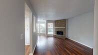 This single-floor residence offers a well-designed layout that balances comfort and functionality throughout. The living area serves as the focal point of the home, showcasing rich, dark hardwood-style flooring that extends across the main living spaces. A striking floor-to-ceiling brick corner fireplace with a white mantel adds warmth and character, while multiple windows invite an abundance of natural light and outdoor views of surrounding greenery.

Adjacent to the living area, the kitchen is equipped with white cabinetry, light countertops, and a full suite of stainless steel appliances, including a refrigerator, range, microwave, and dishwasher. A pass-through window connects the kitchen to the living space, enhancing the open feel of the home.

The bedrooms are carpeted for comfort and feature corner or single-window configurations that bring in natural light. The primary bedroom includes direct access to a dedicated bathroom with a vanity, large mirror, and white cabinetry. A second full bathroom features a tiled tub-shower combination, toilet, and matching vanity. Throughout the home, neutral gray walls, textured ceilings, and clean white trim create a cohesive, move-in-ready aesthetic.
