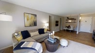 Located at 800 Cottman Avenue in Philadelphia, PA, this single-floor property offers a thoughtfully designed layout that balances comfort and functionality. The living area is open and inviting, featuring warm-toned walls, wood-style flooring, and a seamless flow into the dining space. A large sectional sofa anchors the living room, complemented by tasteful décor, including bold wall art in navy, gold, and gray tones that add a modern yet cozy character to the space. Soft area rugs contrast beautifully with the hardwood-style floors, adding texture and warmth underfoot. A round, dark-wood coffee table serves as a stylish focal point in the living area. The space opens naturally into a dedicated dining area, where a pendant light fixture hangs above a dining table surrounded by upholstered chairs. Open shelving along the dining room wall provides both decorative and practical storage, adding a contemporary touch. The neutral color palette and warm lighting throughout create a cohesive and welcoming ambiance. The single-floor layout ensures easy navigation and accessibility, making this property a comfortable and well-appointed space suited for everyday living.