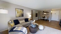 Located at 800 Cottman Avenue in Philadelphia, PA, this single-floor property offers a thoughtfully designed layout that balances comfort and functionality. The living area is open and inviting, featuring warm-toned walls, wood-style flooring, and a seamless flow into the dining space. A large sectional sofa anchors the living room, complemented by tasteful décor, including bold wall art in navy, gold, and gray tones that add a modern yet cozy character to the space. Soft area rugs contrast beautifully with the hardwood-style floors, adding texture and warmth underfoot. A round, dark-wood coffee table serves as a stylish focal point in the living area. The space opens naturally into a dedicated dining area, where a pendant light fixture hangs above a dining table surrounded by upholstered chairs. Open shelving along the dining room wall provides both decorative and practical storage, adding a contemporary touch. The neutral color palette and warm lighting throughout create a cohesive and welcoming ambiance. The single-floor layout ensures easy navigation and accessibility, making this property a comfortable and well-appointed space suited for everyday living.