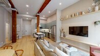 This thoughtfully designed 2-bedroom, 1-bathroom residence seamlessly merges industrial heritage with contemporary style across a single floor. The open-concept layout connects the kitchen, dining, and living areas into a cohesive, light-filled space anchored by striking exposed timber columns and overhead beams that lend warmth and character throughout.

The kitchen is a standout feature, outfitted with sage-green flat-front cabinetry extending to the ceiling, white subway tile backsplash, stainless steel appliances, and a compact dining table ideal for casual meals. The living area is inviting and well-proportioned, with built-in floating shelves, an arched doorway leading to a private outdoor access point, and a curated gallery wall of white architectural plaster pieces that adds artistic flair.

Light hardwood flooring runs throughout, unifying the spaces and enhancing the bright, airy atmosphere. A built-in bench dining nook with pendant lighting creates an additional gathering spot within the main living zone.

Both bedrooms are tranquil retreats, finished in warm neutral tones with tall ceilings, closets, and continued hardwood flooring. The bathroom features terrazzo tile flooring, a floating wood vanity, and clean, modern fixtures. Overall, the residence offers a refined yet comfortable living experience with a distinctive architectural personality.