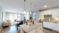 This thoughtfully designed 2-bedroom, 1-bathroom single-floor residence offers a seamless open-concept layout that connects the kitchen, dining, and living areas into one cohesive, light-filled space. The kitchen is a standout feature, showcasing crisp white cabinetry, a herringbone tile backsplash, stainless steel appliances, and a granite-topped island with bar seating, illuminated by a trio of sleek pendant lights. Wood-look flooring runs throughout, adding warmth and continuity to the space. The dining area comfortably accommodates a full-sized table, while the living room opens to the outdoors through glass French doors that flood the space with natural light and provide views of the surrounding community. Both bedrooms are generously proportioned, each featuring ceiling fans, natural light from well-placed windows, and hardwood-style flooring. The primary bedroom connects directly to the shared bathroom, which includes a marble-tiled soaking tub and a walk-in closet with built-in shelving and hanging rods. A second spacious walk-in closet provides additional storage. The bathroom features granite countertops and clean, modern finishes. Overall, the space presents a bright, contemporary aesthetic with functional design throughout.