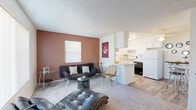 Located at 9777 N Thornydale Rd in Tucson, Arizona, this single-floor unit offers a well-organized and functional layout that makes efficient use of its space. The living area is bright and welcoming, featuring plush carpeting, a textured ceiling, and two windows with vertical blinds that allow natural light to filter in. A warm terracotta accent wall adds a distinct visual element to the room, creating a cozy yet modern ambiance.

The living space flows seamlessly into the kitchen, which is designed with white cabinetry, a white refrigerator, a dishwasher, and a peninsula counter that doubles as a breakfast bar. Wood-look flooring runs throughout the kitchen and dining area, providing a clean contrast to the carpeted living space. A ceiling fan overhead adds to the comfort of the kitchen and dining zone.

The bathroom is clean and practical, featuring a tub-shower combination with tile surround and a curtain rod. Wood-look flooring continues here, and notably, an in-unit washer is conveniently located within or adjacent to the bathroom, adding a practical amenity to daily living.

Overall, the unit presents a straightforward and functional design with a neutral color palette accented by warm tones, making it a comfortable and move-in-ready residence in the northwest Tucson area.