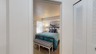 This single-floor residence offers a thoughtfully designed layout encompassing multiple living spaces finished with neutral tones and carpet flooring throughout the main areas. The living room is a standout space, featuring vaulted ceilings that enhance the sense of openness, large sliding glass doors, and an adjacent window that together flood the room with natural light and provide outdoor views. The dining area sits adjacent to the living room, illuminated by a modern chandelier and connected to a pass-through shelf that links it to the kitchen. The kitchen is well-equipped with white cabinetry, granite-style countertops, stainless steel appliances including a range, microwave, dishwasher, and refrigerator, and light tile flooring. The primary bedroom features carpeted floors, a window with outdoor views, and direct access to a walk-in closet. A second bedroom mirrors the carpeted finish, includes a window, and offers a wall-mounted mirror as a notable detail. The bathroom includes a full tub and shower combination with clean white surrounds. Overall, the space maintains a cohesive, comfortable aesthetic with practical finishes throughout.