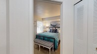 This single-floor residence offers a thoughtfully designed layout encompassing multiple living spaces finished with neutral tones and carpet flooring throughout the main areas. The living room is a standout space, featuring vaulted ceilings that enhance the sense of openness, large sliding glass doors, and an adjacent window that together flood the room with natural light and provide outdoor views. The dining area sits adjacent to the living room, illuminated by a modern chandelier and connected to a pass-through shelf that links it to the kitchen. The kitchen is well-equipped with white cabinetry, granite-style countertops, stainless steel appliances including a range, microwave, dishwasher, and refrigerator, and light tile flooring. The primary bedroom features carpeted floors, a window with outdoor views, and direct access to a walk-in closet. A second bedroom mirrors the carpeted finish, includes a window, and offers a wall-mounted mirror as a notable detail. The bathroom includes a full tub and shower combination with clean white surrounds. Overall, the space maintains a cohesive, comfortable aesthetic with practical finishes throughout.