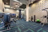 This fitness center in Atlanta's 30326 district is a thoughtfully designed, multi-zone facility that caters to a wide range of workout needs. The space is divided into distinct areas, each purpose-built for a specific type of training. A standout cardio zone features floor-to-ceiling glass walls that flood the area with natural light and offer open views of the surrounding outdoor space, creating an energizing atmosphere during workouts. Treadmills, ellipticals, and step machines are arranged to maximize the views and airflow in this bright, airy section.

The strength training area is anchored by a comprehensive dumbbell rack, multiple adjustable benches, and cable machines, including Matrix-branded equipment. Full-length mirrors line the walls, amplifying the sense of space and allowing users to monitor their form. A dedicated functional training alcove houses medicine balls, kettlebells, a balance ball, and a cable crossover station, set against a decoratively perforated accent wall that adds architectural interest.

Throughout the facility, a bold blue-and-teal geometric carpet ties the zones together visually. Recessed lighting and wall-mounted flat-screen TVs complete the polished, modern aesthetic of this well-appointed fitness space.