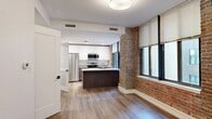 Located at 112 W Adams St in the heart of downtown Jacksonville, Florida, this single-floor unit masterfully combines historic architectural character with contemporary design. Exposed red brick columns and accent walls serve as striking focal points throughout the open living area, paying homage to the building's heritage while contrasting beautifully with the clean white walls and light hardwood-style flooring.

The open-concept kitchen is a standout feature, outfitted with white upper cabinetry, dark lower cabinets, granite countertops, and a full suite of stainless steel appliances including a refrigerator, range, and microwave. A central island with a built-in sink provides additional workspace and casual dining potential. Large windows fitted with roll-up shades line the living area, drawing in generous natural light and offering views of the surrounding urban streetscape.

The bedroom area is bright and well-proportioned, with the same large windows and a sleek sliding glass-panel door that adds a modern industrial touch. The bathroom is cleanly finished with white subway-tiled tub surround, a granite-topped dark wood vanity, and neutral tile flooring, creating a crisp, spa-like feel. Throughout the unit, thoughtful detailing and quality finishes deliver a refined yet functional living environment in the heart of Jacksonville's downtown core.