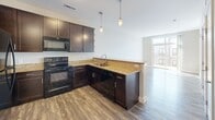 This thoughtfully designed one-bedroom, one-bathroom unit offers an efficient and comfortable single-floor layout. The kitchen serves as a standout feature, showcasing rich dark cabinetry, striking granite countertops, a peninsula with pendant lighting, and a full suite of black appliances including a refrigerator, range, microwave, and dishwasher. The kitchen flows naturally into the living area, which benefits from large sliding glass doors that invite abundant natural light and provide direct access to a private balcony with views of the surrounding building exterior. Hardwood-style flooring runs throughout the main living and kitchen areas, adding warmth and cohesion to the space. The bedroom is a comfortable retreat finished with plush carpeting, a ceiling fan, and its own sliding glass door access to the balcony, further extending the sense of space. A dedicated closet offers convenient storage directly off the bedroom. The bathroom continues the upscale design language with a granite vanity countertop, an undermount sink, brushed nickel fixtures, and a large wall mirror. Neutral tones throughout the unit create a clean, modern aesthetic that is both inviting and easy to personalize.