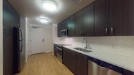 Located on the fifth floor at 1133 SW Market St in Portland's vibrant SW neighborhood, Unit 507 is a thoughtfully designed apartment that combines modern finishes with a functional, open layout. The kitchen serves as a standout feature, outfitted with dark espresso cabinetry that extends to the ceiling for ample storage, light quartz countertops, a herringbone-patterned tile backsplash, and a full suite of stainless steel appliances including a gas range, built-in microwave, refrigerator, and dishwasher. Warm wood-tone flooring runs throughout the unit, creating a cohesive and inviting atmosphere. The kitchen flows seamlessly into an open living area, offering a versatile space that can be configured to suit a variety of layouts. The bedroom provides a quiet retreat complete with a sliding-door closet offering built-in shelving and hanging storage. The bathroom features a clean, bright design with a full soaking tub and shower combination, chrome fixtures, and a dark-cabinetry vanity with a light countertop. Flush-mount ceiling lighting throughout the unit ensures consistent illumination in every room. The unit's efficient floor plan makes excellent use of space, delivering a polished urban living experience in the heart of Portland.