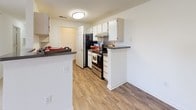 This single-floor residence offers a thoughtfully organized layout designed for comfortable everyday living. The kitchen is outfitted with white cabinetry, dark countertops, stainless steel appliances including a range and refrigerator, and wood-style flooring that extends throughout the common areas, giving the space a cohesive and clean aesthetic. A peninsula-style counter provides additional workspace and separation from the adjoining living area, which is equipped with a ceiling fan. The bedrooms are carpeted in a neutral tone, promoting a warm and quiet atmosphere. Natural light filters through large windows fitted with horizontal blinds, offering pleasant outdoor views of surrounding greenery. A notable feature of the primary bedroom is the dual closets, each equipped with wire shelving, providing generous storage capacity. Both bathrooms mirror each other in design, featuring wood-style flooring, white vanity cabinetry with dark countertops, large mirrors, and well-lit vanity lighting. A dedicated laundry area houses an in-unit top-loading washer along with wire shelving above for additional storage. Throughout the space, crisp white walls and clean finishes create a bright, neutral backdrop that is both practical and easy to personalize.
