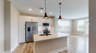 Located at 100 Fulton St SE in Atlanta, GA, this single-floor residence combines modern design with functional living spaces. The open-concept kitchen serves as the heart of the home, showcasing white shaker-style cabinetry with matte black hardware, quartz countertops, and a large central island with an undermount sink. Stainless steel appliances — including a side-by-side refrigerator with ice dispenser, built-in microwave, and range — complement the clean aesthetic, while bronze pendant lights add warmth overhead. A built-in pantry with open shelving provides generous storage just off the kitchen.

The living area is bright and airy, featuring wide-plank wood-look flooring, large windows with ample natural light, and views of the surrounding Atlanta greenery. The bedroom offers plush carpeting, a ceiling fan, and a well-sized window that continues the theme of natural light throughout.

Bathrooms are finished with wood-look tile flooring, white vanities with quartz countertops, and matte black fixtures. The primary bathroom includes a glass-enclosed walk-in shower and a dual-sink vanity, while the secondary bath features a full tub-shower combo. An in-unit laundry area with a stacked washer and dryer rounds out this thoughtfully designed residence.