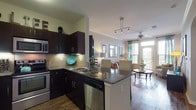 This single-story, one-bedroom, one-bathroom residence offers a thoughtfully designed open-concept layout that seamlessly connects the kitchen, dining, and living areas. The kitchen is a standout feature, equipped with dark espresso cabinetry, stainless steel appliances including a range, microwave, and dishwasher, a tile backsplash, and dark granite countertops that extend to a peninsula breakfast bar. Track lighting overhead adds a modern touch.

The living area is bright and inviting, featuring hardwood-style flooring, crown molding, and a ceiling fan. Large windows and a glass-panel door lead to a private balcony, filling the space with natural light and offering outdoor views.

The bedroom is comfortably sized with a ceiling fan, a large window with outdoor views, and hardwood-style flooring. It includes a walk-in closet with built-in shelving for ample storage.

The bathroom features tile flooring, a full soaking tub and shower combination with tile surround, a granite-topped vanity, and a built-in linen shelving niche, providing practical storage within a clean, neutral aesthetic throughout.