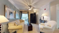 Located at 1001 Bear Island Rd in Summerville, South Carolina, this single-floor residence offers a thoughtfully designed layout with a warm and welcoming ambiance throughout. The kitchen is equipped with light wood cabinetry, black appliances including a full-size refrigerator and built-in microwave, a double sink, and a peninsula with a breakfast bar that opens to the main living area. A dedicated built-in workspace adjacent to the kitchen features ample cabinetry and a generous countertop surface, ideal for a home office setup. The living room is bright and comfortable, highlighted by a vaulted ceiling with a ceiling fan, soft blue accent walls, crown molding, large sliding glass doors that invite natural light, and plush carpeting underfoot. The primary bedroom offers a serene retreat with a neutral accent wall, natural light from a large window with outdoor views, and soft carpeting. The second bedroom makes a bold statement with a vibrant red accent wall, a walk-in closet, and bright windows. Both bathrooms are finished with tile flooring, vanity mirrors, and tub-shower combinations. Consistent crown molding and track lighting throughout the common areas lend a polished, cohesive feel to the entire space.