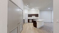 This thoughtfully laid-out one-bedroom, one-bathroom unit offers a cohesive and modern living experience across a single floor. The open-concept kitchen and living area serves as the heart of the space, featuring rich dark-wood cabinetry with sleek silver hardware, a white quartz countertop, a subway tile backsplash, and a central island that provides additional prep and seating space. Stainless steel appliances, including a refrigerator, range, microwave, and dishwasher, complete the kitchen's functional and contemporary aesthetic. Light wood laminate flooring runs continuously throughout the unit, creating a warm, unified feel. The living area is bright and open, illuminated by recessed lighting and a ceiling fan. The generously sized bedroom features dual windows with blinds that allow natural light to filter in, a ceiling fan, and direct access to a full bathroom and a dedicated walk-in closet. The closet is equipped with wire shelving for organized storage. The bathroom includes a full soaking tub with a white tile surround and a curved shower rod. Clean white walls throughout the unit enhance the sense of openness and provide a neutral backdrop adaptable to any style.