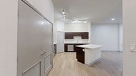 This thoughtfully laid-out one-bedroom, one-bathroom unit offers a cohesive and modern living experience across a single floor. The open-concept kitchen and living area serves as the heart of the space, featuring rich dark-wood cabinetry with sleek silver hardware, a white quartz countertop, a subway tile backsplash, and a central island that provides additional prep and seating space. Stainless steel appliances, including a refrigerator, range, microwave, and dishwasher, complete the kitchen's functional and contemporary aesthetic. Light wood laminate flooring runs continuously throughout the unit, creating a warm, unified feel. The living area is bright and open, illuminated by recessed lighting and a ceiling fan. The generously sized bedroom features dual windows with blinds that allow natural light to filter in, a ceiling fan, and direct access to a full bathroom and a dedicated walk-in closet. The closet is equipped with wire shelving for organized storage. The bathroom includes a full soaking tub with a white tile surround and a curved shower rod. Clean white walls throughout the unit enhance the sense of openness and provide a neutral backdrop adaptable to any style.