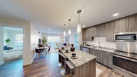 This well-appointed single-floor residence offers a thoughtfully designed open-concept layout that seamlessly connects the kitchen, dining, and living areas into one cohesive, light-filled space. The kitchen is a standout feature, showcasing wood-grain cabinetry in a warm gray-brown tone, granite countertops, and a full suite of stainless steel appliances including a refrigerator, range, microwave, and dishwasher. A large central island with granite counters and bar seating serves as both a functional workspace and a social hub, illuminated by a trio of elegant pendant lights. Rich hardwood-style flooring runs throughout the main living areas, adding warmth and continuity. The living room is bright and inviting, anchored by large sliding glass doors that open to a private balcony and allow abundant natural light to fill the space. The primary bedroom is generously sized with large windows and ample closet space, while the second bedroom offers a cozy, well-lit retreat. Two bathrooms serve the residence — one featuring a granite-topped vanity and the other a full tub-shower combination — both finished with coordinating wood-tone cabinetry and hardwood-style flooring. The overall design aesthetic is clean, modern, and cohesive throughout.