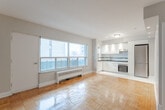 This 350 square foot apartment, located at 87 Jameson Ave in Toronto, offers a thoughtfully designed living space within a single floor. The open-concept layout seamlessly integrates the kitchen and living room, maximizing the use of available space. The apartment boasts beautiful parquet flooring throughout, adding warmth and character to the interior.

The kitchen is a standout feature, equipped with modern white cabinetry, stainless steel appliances, and sleek black countertops. A tile backsplash with a decorative black stripe adds a touch of elegance. The kitchen floor features a distinctive mosaic tile pattern, creating a visual separation from the living area.

Large windows dominate one wall of the living room, flooding the space with natural light and offering views of the surrounding area. A glass door leads to a small balcony, extending the living space outdoors. A baseboard heater beneath the window ensures comfort during colder months.

The bathroom, while compact, is well-appointed with a full-sized bathtub and shower combination. White tiles with a black accent stripe echo the kitchen's design, while a mosaic floor ties the spaces together visually. A modern vanity with a dark countertop provides storage and completes the bathroom's contemporary look.

Despite its modest size, the apartment's intelligent design and use of light colors create an open, airy feel throughout, making it an ideal urban dwelling in the heart of Toronto.