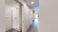 Located at 757 N Grant St in Denver's Capitol Hill neighborhood, this efficiently designed single-floor unit offers a clean, contemporary aesthetic throughout. The open-plan living room and kitchen area is anchored by large windows that flood the space with natural light and frame views of the surrounding urban streetscape, complemented by a wall-mounted HVAC unit and smooth hardwood-style flooring in a cool gray tone.

The kitchen is well-appointed with light maple cabinetry extending to the ceiling for ample storage, a full suite of stainless steel appliances including a range, over-the-range microwave, and dishwasher, plus a subway tile backsplash and white countertops. A dedicated pantry provides additional storage conveniently accessible from the kitchen area.

A hallway connects the living spaces to the bathroom and utility area, where an in-unit washer and dryer are tucked neatly behind a panel. The bathroom features a glass-enclosed walk-in shower with tile surround, wood-toned vanity cabinetry, and the same durable hardwood-style flooring found throughout the unit.

Recessed lighting, crisp white walls, and a cohesive modern design language give the entire space a bright, polished feel that makes efficient use of every square foot.