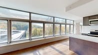 Located at 100 Reserve Road in Danbury, CT, this thoughtfully designed one-bedroom, one-bathroom residence offers a modern aesthetic with high-quality finishes throughout. The open-concept living and kitchen area is the heart of the home, defined by a dramatic wall of floor-to-ceiling windows that flood the space with natural light and frame picturesque views of the surrounding tree-lined landscape. Warm hardwood flooring runs continuously throughout, enhancing the cohesive and inviting atmosphere.

The kitchen is efficiently designed with dark cabinetry, stainless steel appliances including a range, microwave, and dishwasher, white quartz countertops, and a classic subway tile backsplash. A peninsula provides additional workspace and separation between the kitchen and living area.

The spacious bedroom features the same warm hardwood floors, clean white walls, a wall-mounted climate control unit, and two closets, offering generous storage. Sunlight filters in to create a bright, comfortable retreat.

The full bathroom is finished in a clean, contemporary style, featuring a soaking tub with shower, a vanity with storage, and hardwood flooring that continues the design language of the rest of the home. An entrance area completes the layout, providing a functional transition into the living space.