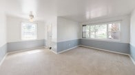 Located at 1201 E San Miguel St in Colorado Springs, Colorado, this single-story unit presents a cohesive and practical interior design throughout. A distinctive two-tone wall treatment — soft blue-gray on the lower half and crisp white above — runs consistently through the living areas and bedrooms, lending a unified aesthetic to the space. Neutral-toned carpeting underfoot complements this palette, while ceiling light fixtures provide overhead illumination in each room.

The living area is generously sized, benefiting from multiple windows that draw in natural light and offer views of the mature trees outside. The layout, as seen in the floor plan, flows efficiently between rooms, with multiple doorways connecting the living spaces to the bedrooms and service areas.

The kitchen features dark speckled countertops contrasting with bright white cabinetry, a single-basin sink, and a classic black-and-white checkered tile floor. A barred window above the counter provides natural light and outdoor views of the surrounding greenery.

The bathroom carries the same black-and-white theme, with tiled walls accented by black borders, a full tub-shower combination, a pedestal sink, and matching checkered flooring, creating a clean, timeless look throughout.