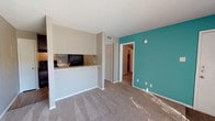 Located at 4625 71st St in Lubbock, Texas, this single-story unit offers a practical and comfortable layout designed for everyday living. The open living area is finished with neutral-toned carpet and is anchored by a bold teal accent wall that adds a pop of color to the otherwise neutral palette. A full-width sliding glass door fitted with vertical blinds floods the space with natural light and provides views of the surrounding exterior.

The kitchen is accessible via a pass-through counter with granite-style laminate surfaces, offering a convenient connection to the living area. Inside the kitchen, dark espresso cabinetry is paired with black appliances, including a coil-top range with overhead ventilation, a full-size refrigerator, and a dishwasher, all set atop wood-look flooring that contrasts with the cabinetry.

The bathroom features a tub-shower combination with white tile surround, a granite-topped vanity with an undermount sink, and brushed nickel hardware and towel bar. Textured ceilings are present throughout the unit, contributing to its classic residential character. Closet space is accessible from the main living corridor, and the overall layout is efficient and well-connected across each area of the home.