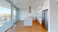 Located at 915 W Grape St in San Diego's vibrant Little Italy neighborhood, this modern single-floor unit showcases a clean, contemporary design with warm hardwood flooring flowing seamlessly throughout every room. The expansive open-concept living area is bathed in natural light, courtesy of floor-to-ceiling windows and sliding glass doors that open to a balcony offering sweeping city and harbor views. The sleek, modern kitchen features a large central island with an integrated cooktop, a stainless steel range hood, white cabinetry, quartz countertops, and stainless steel appliances including a refrigerator and dishwasher. The spacious bedrooms are well-lit by oversized windows, with one featuring a generously sized walk-in closet equipped with built-in shelving and hanging rods. Two bathrooms maintain the home's clean aesthetic — one with a soaking tub and subway tile surround, and another with a wide vanity and a large mirror. A hallway utility closet houses a stacked washer and dryer for added convenience. Recessed lighting throughout completes the refined, minimalist ambiance of this thoughtfully designed urban residence.