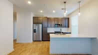 This well-designed single-floor unit offers a contemporary living experience with thoughtful finishes throughout. The heart of the space is a modern kitchen, outfitted with rich dark-toned cabinetry reaching to the ceiling for ample storage, sleek white countertops, and a full suite of stainless steel appliances including a side-by-side refrigerator with ice and water dispenser, electric range, and over-the-range microwave. A white subway tile backsplash adds a clean, classic accent, while a central island with an integrated sink and pendant lighting above serves as both a functional workspace and a natural gathering point. Warm wood-look flooring extends seamlessly throughout the unit, contributing to a cohesive and inviting aesthetic. The bedrooms are bright and well-proportioned, each featuring a ceiling fan and large windows dressed with blinds that allow for natural light and outdoor views. The primary suite connects to a generously sized walk-in closet equipped with wire shelving systems for organized storage. The primary bathroom features dark wood vanity cabinetry, a white countertop with a dual-sink setup, a large mirror, and a direct passthrough to the walk-in closet, creating a practical and comfortable private retreat. Recessed lighting throughout enhances the clean, modern atmosphere of the entire space.