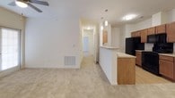 This single-floor residence offers a thoughtfully designed layout that balances comfort and functionality. The open-concept living area features soaring ceilings, neutral-toned carpet, and a ceiling fan, creating a bright and airy atmosphere. A half-wall peninsula seamlessly connects the living space to the kitchen, which is finished with warm medium-tone wood cabinetry, granite-look countertops, and light hardwood-style flooring. The kitchen is fully equipped with black appliances, including a refrigerator, range, microwave, and dishwasher, along with ample counter and cabinet space. Pendant lighting above the peninsula adds a polished touch. A hallway leads to the private areas of the home, where carpeted bedrooms each include a ceiling fan and windows that allow natural light to filter in. The bathroom is finished with matching wood cabinetry, granite-look countertops, a large mirror, and hardwood-style flooring, alongside a full tub and shower combination. Storage is a standout feature, with a spacious walk-in closet offering multiple hanging rods and shelving, complemented by an additional reach-in closet with built-in shelving in a secondary bedroom. Consistent warm, neutral tones and cohesive finishes throughout give the space a clean, move-in-ready appeal.