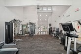 This state-of-the-art gym facility, located at 9200 Willow Ridge in Charlotte, NC, offers an impressive 1,730 square feet of fitness space. The single-story building is characterized by its modern design and functional layout. Upon entry, visitors are greeted by a welcoming foyer with sleek wood-look flooring and French doors that flood the space with natural light.

The gym's interior is notable for its vaulted ceilings, which create a sense of openness and airiness. Skylights and large windows further enhance the bright, inviting atmosphere. The main workout area is divided into distinct zones, catering to various fitness needs. A well-equipped cardio section features treadmills and elliptical machines, while the strength training area boasts a comprehensive selection of weight machines and free weights.

The facility's design incorporates both practicality and aesthetics, with clean white walls, recessed lighting, and strategically placed mirrors to enhance the sense of space. Additional amenities include storage solutions for personal belongings and informational signage to guide users. The gym's layout promotes easy navigation and efficient use of space, making it an ideal environment for fitness enthusiasts of all levels.