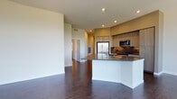 This contemporary single-floor residence offers a thoughtfully designed open-concept layout with clean lines and modern finishes. Dark hardwood flooring flows throughout the space, providing a rich contrast against the crisp white walls and creating a cohesive, polished aesthetic.

The kitchen is a standout feature, anchored by a curved island with a sleek dark quartz countertop and white base. It is fully equipped with stainless steel appliances — including a French door refrigerator, a range with oven, a built-in microwave, and a dishwasher — all complemented by warm wood-toned cabinetry that extends to the ceiling. Recessed lighting illuminates the space, adding depth and warmth.

The open living area flows naturally from the kitchen and is bathed in natural light through large floor-to-ceiling windows that offer elevated outdoor views of the surrounding neighborhood. The bedrooms are generously proportioned, each featuring dark hardwood floors, large windows, and ceiling fans for year-round comfort.

The bathrooms are finished to a high standard, featuring wood-grain vanities with quartz countertops, under-mount sinks, and illuminated mirrors. One bathroom includes a soaking tub with tile surround, while another connects to a walk-in closet with built-in wire shelving. The overall ambiance of the residence is modern, bright, and move-in ready.