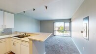 Located at 7484 E 29th Ave in Denver's Central Park neighborhood, this single-floor unit offers a functional and open layout designed to maximize livable space. The open-concept living and kitchen area serves as the heart of the unit, where carpet flooring in the living space transitions to hardwood in the kitchen. Large sliding glass doors flood the living area with natural light and provide views of the surrounding neighborhood and greenery beyond.

The kitchen is well-equipped with white cabinetry offering ample storage, a decorative tile backsplash, white appliances including a refrigerator, electric range, microwave, and dishwasher, and a peninsula countertop that defines the boundary between the kitchen and living areas. Recessed and track lighting illuminate the space effectively.

The bedrooms are carpeted and feature windows that bring in natural light, with one room offering access to a closet. The bathroom is finished in a clean, bright palette with wood-look flooring, a single-sink vanity with white cabinetry, and a elongated layout that leads to additional storage and laundry space. Overall, the unit presents a straightforward, light-filled interior with practical finishes throughout.