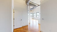 Located at 219 N Columbus St in Lancaster, Ohio, this 2-bedroom, 2-bathroom loft-style unit delivers an impressive blend of industrial character and modern finishes. Soaring ceilings with exposed ductwork and painted brick walls set a distinctly urban tone throughout the open living space, while warm hardwood floors add richness underfoot. Large black-framed windows flood the interior with abundant natural light and offer views of the surrounding cityscape and greenery.

The kitchen and living area form a generous open-plan layout anchored by a sleek center island with light quartz countertops. White shaker cabinetry, stainless steel appliances—including a refrigerator with ice maker, electric range, microwave, and dishwasher—and industrial-style pendant lighting complete the well-appointed kitchen.

The spacious primary bedroom continues the loft aesthetic with soaring ceilings, exposed brick, and ample natural light through oversized windows. The second bedroom offers hardwood flooring and bright, clean walls. A dedicated closet provides additional storage.

Both bathrooms are finished with hexagonal mosaic tile flooring and white subway tile. The primary bath features a sliding glass-door walk-in shower with a dark metal frame, while the second bath offers a full soaking tub and shower combination. The overall ambiance is open, airy, and stylishly industrial.