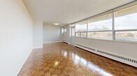 This thoughtfully laid-out 1-bedroom, 1-bathroom unit spans a single floor and offers a comfortable, functional living environment. The space is defined throughout by polished parquet wood flooring in a classic herringbone-style pattern, lending warmth and character to every room.

The spacious living room is a standout feature, lined with large floor-to-ceiling windows that flood the space with natural light and offer sweeping outdoor views of the surrounding treetops and sky. A baseboard heating system runs beneath the windows, ensuring year-round comfort. The open sightline from the hallway into the living area enhances the sense of space.

The kitchen has been updated with white shaker-style cabinetry, subway tile backsplash, stone countertops, and full-sized stainless steel appliances including a French door refrigerator and dishwasher. Light-toned flooring complements the clean, modern aesthetic.

The bedroom is generously sized, featuring its own large window with outdoor views, a ceiling fan, and the same polished parquet flooring found throughout the unit. The bathroom is finished with crisp white subway tile surrounding a full soaking tub and shower combination, paired with chrome fixtures for a clean, timeless look.

A connecting hallway ties all rooms together efficiently, completing this well-organized and bright living space.