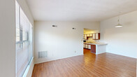 This 2-bedroom, 1-bathroom single-floor unit offers a functional and straightforward layout designed for comfortable everyday living. The open living room greets you with warm hardwood-style flooring that flows throughout the main areas, clean white walls, and a large window that allows natural light to brighten the space. The room connects seamlessly to the kitchen via a convenient pass-through peninsula counter, making the area feel open and well-connected.

The kitchen is equipped with wood-trimmed white cabinetry, light countertops, a double sink, and white appliances including a refrigerator, electric range, and dishwasher. A hallway leads from the kitchen toward the rest of the unit, providing an efficient flow between rooms.

Both bedrooms are carpeted for comfort, each featuring windows with blinds that bring in natural light and offer views of surrounding greenery. The primary bedroom is a comfortable size, while the second bedroom is well-proportioned and versatile.

The bathroom is clean and functional, featuring a full soaking tub with a shower, curtain rod, and standard fixtures. A dedicated closet provides additional storage within the unit. The overall ambiance is bright, neutral, and move-in ready.