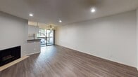 Located at 320 S Arnaz Drive in the heart of Los Angeles, this single-floor unit offers a clean, modern aesthetic throughout. The open living area is finished with smooth hardwood-style flooring and crisp white walls, illuminated by recessed lighting and a ceiling fan that enhances comfort and airflow. A sliding glass door leads to a private balcony, where lush tree canopies provide a serene, green backdrop — a notable feature that brings natural light and outdoor connection into the living space.

The kitchen is efficiently designed and features stainless steel appliances, including a full-size refrigerator, gas range, and microwave. Dark stone countertops contrast neatly against white cabinetry, creating a polished, functional workspace. A wall-mounted air conditioning unit ensures climate control year-round.

The bedroom is a quiet, neutral-toned retreat with the same warm hardwood-style flooring, recessed lighting, and access to a walk-in closet area. The bathroom is clean and straightforward, offering a glass-enclosed shower and classic white fixtures. Smooth gray walls and chrome hardware lend a cohesive, contemporary feel throughout the space, making this unit a well-appointed option in a desirable Los Angeles neighborhood.