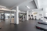 Located at 417 Centinela Ave in Inglewood, California, this fitness center offers a generously sized, single-floor exercise space designed to support a comprehensive workout experience. The interior features a clean, modern aesthetic with crisp white walls, white structural columns, and durable rubber flooring throughout, creating a professional gym environment.

The space is thoughtfully organized into distinct training zones. A dedicated cardio area houses treadmills and stationary cycling bikes, while a strength training section offers a variety of cable and weight machines, including Hoist-branded equipment. A free weights zone features neatly arranged dumbbell racks alongside a full-length mirrored wall, which enhances the sense of space and allows for form monitoring during exercise. A "Training Zone" designation is posted in this area for easy navigation.

Natural light filters in through windows along the perimeter, complementing the bright, recessed and linear fluorescent lighting overhead. Motivational wall graphics — including phrases such as "YOUR ONLY LIMIT IS YOU" and a bold "WORKOUT" typography installation — contribute to an energizing atmosphere. Wall-mounted flat-screen televisions are positioned throughout the space for entertainment during workouts. The layout is open and uncluttered, allowing for ease of movement between equipment stations.
