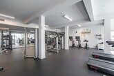 Located at 417 Centinela Ave in Inglewood, California, this fitness center offers a generously sized, single-floor exercise space designed to support a comprehensive workout experience. The interior features a clean, modern aesthetic with crisp white walls, white structural columns, and durable rubber flooring throughout, creating a professional gym environment.

The space is thoughtfully organized into distinct training zones. A dedicated cardio area houses treadmills and stationary cycling bikes, while a strength training section offers a variety of cable and weight machines, including Hoist-branded equipment. A free weights zone features neatly arranged dumbbell racks alongside a full-length mirrored wall, which enhances the sense of space and allows for form monitoring during exercise. A "Training Zone" designation is posted in this area for easy navigation.

Natural light filters in through windows along the perimeter, complementing the bright, recessed and linear fluorescent lighting overhead. Motivational wall graphics — including phrases such as "YOUR ONLY LIMIT IS YOU" and a bold "WORKOUT" typography installation — contribute to an energizing atmosphere. Wall-mounted flat-screen televisions are positioned throughout the space for entertainment during workouts. The layout is open and uncluttered, allowing for ease of movement between equipment stations.