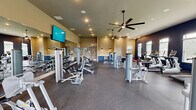 Located at 2411 Wave Rock Way in Knoxville, Tennessee, this well-appointed fitness center offers a generously sized, single-floor exercise facility designed to support a comprehensive workout experience. The space is thoughtfully laid out to accommodate a wide variety of equipment, including multiple strength-training machines, a full dumbbell rack, treadmills, stationary bikes, rowing machines, and cable systems — providing options for both cardiovascular and resistance training.

The interior features durable rubber flooring throughout, ideal for high-traffic fitness use. A large mirrored wall along one side visually expands the space while allowing users to monitor their form. Overhead, multiple large ceiling fans provide consistent airflow, complementing the recessed lighting that keeps the environment bright and energizing. Wall-mounted televisions are positioned for easy viewing during workouts.

The design blends warm beige tones on the main walls with bold navy blue accent walls, creating a dynamic and motivating atmosphere. Numerous windows along the perimeter flood the space with natural light and offer views of the surrounding outdoor greenery. A glass-paneled entry door adds to the openness and accessibility of the facility. The overall ambiance is clean, modern, and purpose-built for fitness — making it a well-equipped destination for residents seeking a convenient and fully featured exercise environment.