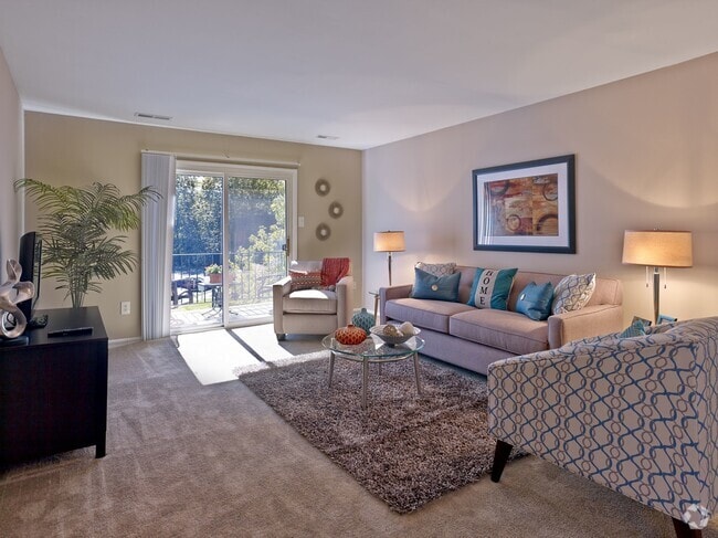 Enjoy a warm and inviting living room at Haynes Run Apartments, featuring plush carpeting, contemporary décor, and access to a private outdoor balcony. - Haynes Run