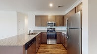 Located at 321 E Park Rd in Indian Trail, NC, this single-floor residence offers a thoughtfully designed layout with a clean, contemporary aesthetic throughout. The kitchen serves as a central highlight, featuring rich medium-toned cabinetry, granite countertops, and a full suite of stainless steel appliances including a range, over-the-range microwave, dishwasher, and refrigerator. A peninsula with a double sink provides additional counter space and casual dining potential, seamlessly connecting the kitchen to the open living area. The living room is generously proportioned, finished with plush neutral carpeting and recessed lighting, and benefits from natural light through a glass-paneled entry door. Bedrooms continue the warm, comfortable feel with soft carpeting, ample closet storage including double-door closets, and bright windows with blinds. The bathroom features warm wood-look vinyl plank flooring, a medium-toned vanity with a white countertop, a tub-shower combination, and brushed nickel fixtures throughout. Crown molding accents the kitchen and living areas, adding a refined architectural detail. The overall palette of whites, warm neutrals, and rich wood tones creates a cohesive and inviting atmosphere throughout the home.