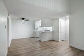 Located at 1750 W Romneya Dr in Anaheim, CA, this single-story 2-bedroom, 1-bathroom home offers a clean, modern aesthetic with thoughtful design details throughout. The living room is a standout space, featuring striking vaulted ceilings with exposed white-painted wood beams that add architectural character and a sense of height. Light wood laminate flooring runs throughout the home, creating a cohesive and warm feel. A sliding glass door in the living area opens to an outdoor view, filling the space with natural light. The kitchen is well-appointed with white cabinetry, light stone-look countertops, a built-in range, and a bright overhead panel light. A peninsula counter connects the kitchen to the adjacent living and dining area, which also features a ceiling fan. The primary bedroom is generously sized, complete with a walk-in closet offering built-in shelving and hanging rods. The second bedroom includes a natural light window and direct hallway access. The bathroom is clean and functional, featuring a full tub-shower combination with white surround. Two closets provide ample storage across the home. The overall palette of crisp white walls and light flooring gives the space a fresh, move-in-ready feel.