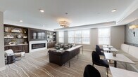Located at 435 Duane St in Glen Ellyn, Illinois, this single-floor community space is designed with a refined, contemporary aesthetic that balances comfort and functionality. The main lounge area serves as the centerpiece, anchored by a sleek linear fireplace set within a dark wood built-in wall unit that houses a large flat-screen television and open shelving with decorative displays. Textured, patterned wallcovering flanks the built-in, adding depth and visual interest to the space.

Seating is thoughtfully arranged throughout, featuring a tufted dark leather sofa paired with upholstered armchairs and an array of tables suited for both casual conversation and focused work. A striking drum chandelier and recessed lighting illuminate the room, complementing the abundant natural light that enters through multiple large windows dressed with clean white blinds. Patterned carpeting with flowing linear motifs adds warmth underfoot.

Adjacent to the lounge, a well-appointed kitchenette features floor-to-ceiling slate-blue cabinetry, white quartz countertops, a mosaic tile backsplash, and small appliances. A separate utility area includes a wet sink with elongated mosaic tile and access to a glass-enclosed wet room, providing additional functionality. The overall ambiance is polished and welcoming throughout.