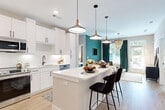 This well-appointed single-floor residence combines contemporary design with functional living. The heart of the home is a sleek, open-concept kitchen outfitted with crisp white shaker cabinetry, black hardware accents, stainless steel appliances, and a generous central island with seating for multiple guests. A trio of modern pendant lights anchors the kitchen, while light wood-tone flooring extends seamlessly into the adjacent living area. The living space is distinguished by a bold teal accent wall, floor-to-ceiling drapery, and access to an outdoor area, creating a vibrant yet inviting atmosphere.

The primary bedroom features plush carpeting, a ceiling fan, and a striking teal accent wall complemented by natural light from a well-positioned window. A second bedroom offers a quieter, neutral palette with warm tones, carpeted flooring, and ample room for a dresser and furnishings. Both bedrooms benefit from dedicated walk-in closets equipped with wire shelving systems that maximize storage capacity.

The bathroom is finished with a white quartz vanity, black-framed mirror, matte black fixtures, and a marble-tiled shower, achieving a clean and modern aesthetic. Throughout the residence, consistent use of light tones, quality materials, and thoughtful design details create a cohesive and comfortable living environment.