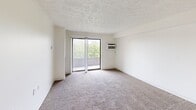 This two-bedroom, one-bathroom apartment in Berkley, Michigan offers a well-organized single-floor layout with a clean, neutral aesthetic throughout. The combined kitchen and living area serves as the heart of the home, where the kitchen stands out with white shaker cabinetry, light countertops, a stainless steel refrigerator, and a gas range. A peninsula counter provides additional workspace and open sightlines into the living area. The living room is carpeted and features a sliding glass door that opens onto a private balcony, inviting natural light and outdoor views of surrounding greenery. A wall-mounted AC unit ensures year-round comfort. Both bedrooms are carpeted with neutral tones and feature large sliding or hinged closets offering ample storage. Natural light filters in through vertical-blind-covered windows in each room. The full bathroom is finished with wood-look vinyl flooring, a white vanity with under-cabinet storage, a large mirror, and a shower-tub combination with grab bars. Textured ceilings are consistent throughout the unit, contributing to the space's classic character. This apartment offers a functional, well-maintained living environment in a residential Berkley neighborhood.